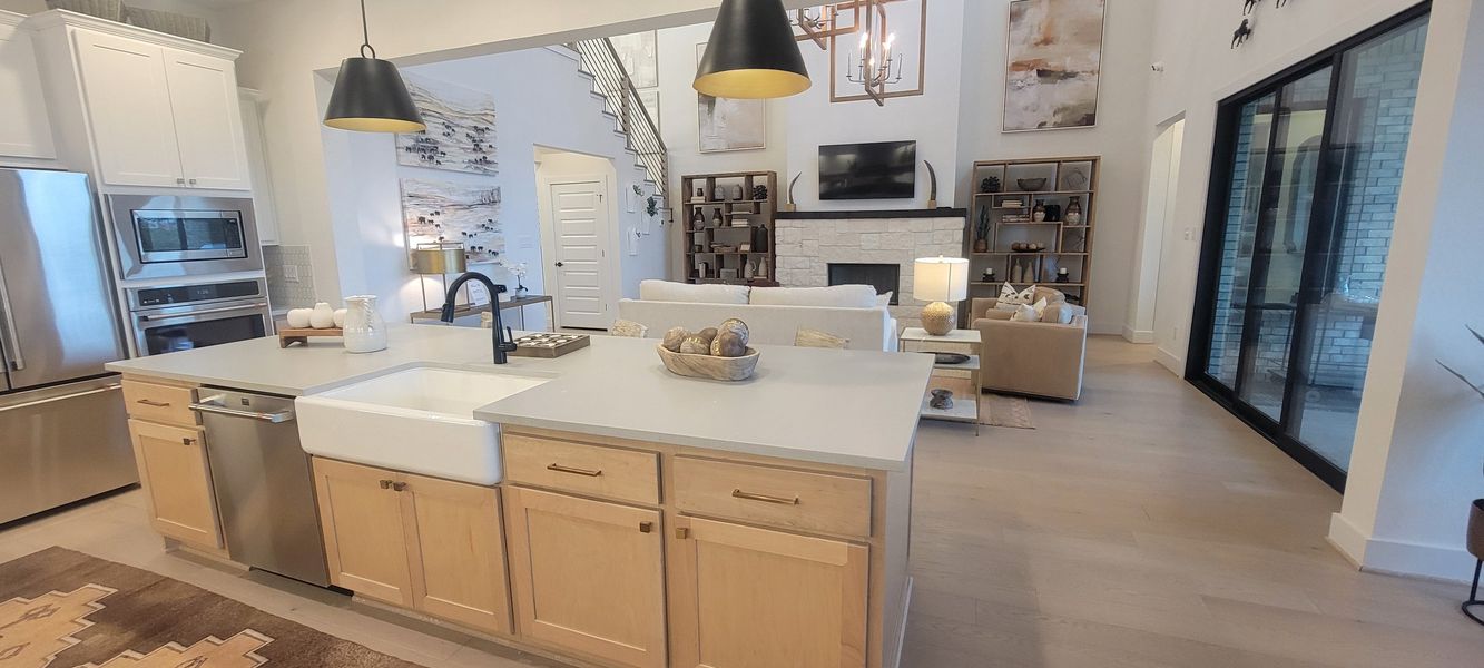 A modern open-concept living space with a sleek kitchen island, farmhouse sink, and cozy seating around a stone fireplace.