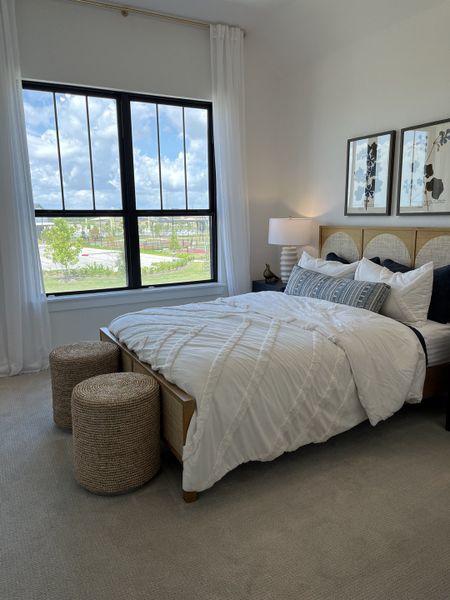 A cozy bedroom with elegant decor, featuring a plush bed, textured stools, and large windows bringing in natural light.