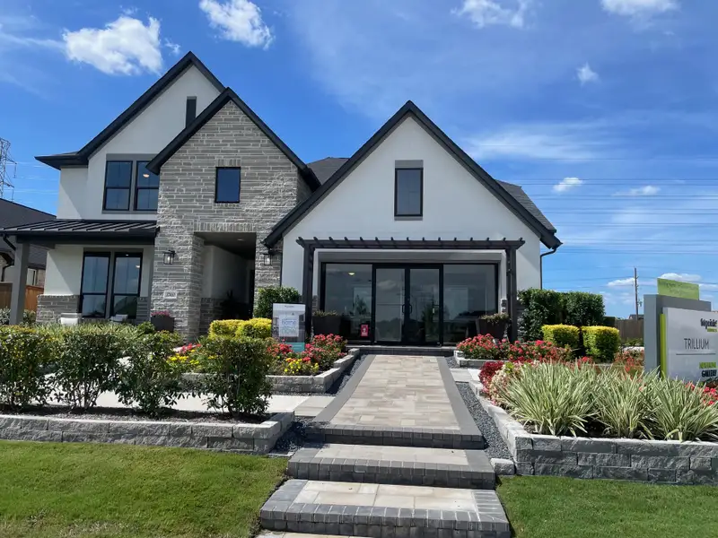 A modern stone and white facade home with lush landscaping in Trillium 40′ by Tri Pointe Homes (Richmond, TX). A modern stone and white facade home with lush landscaping in Trillium 40′ by Tri Pointe Homes (Richmond, TX).
