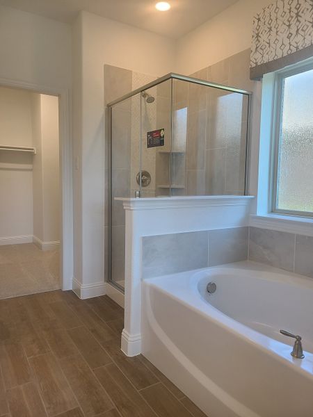 A modern bathroom featuring a glass-enclosed shower, a relaxing tub, and elegant wood-look tile flooring.