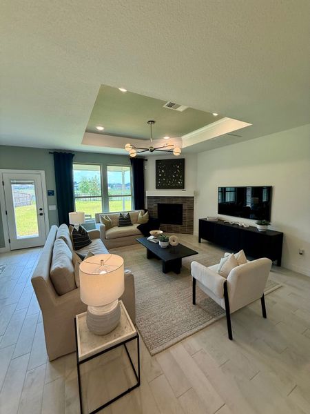 A cozy living room featuring beige sofas, a modern fireplace, and a sleek chandelier with abundant natural light.