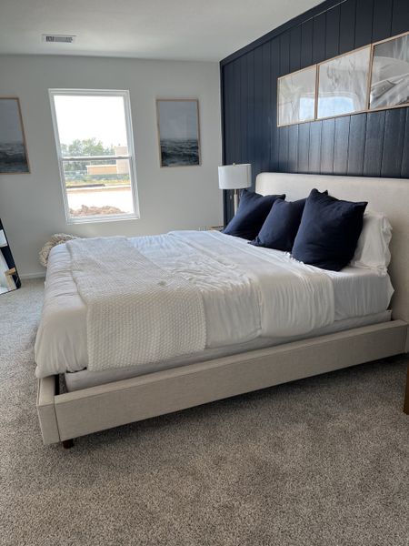 A cozy bedroom with a plush bed, dark accent wall, elegant framed artwork, and soft carpet flooring.