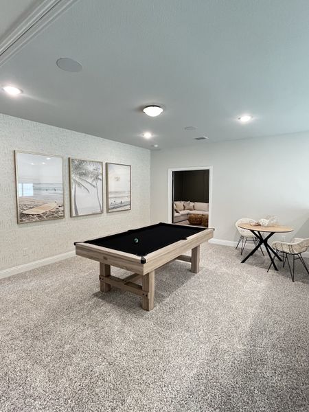 A contemporary game room featuring a sleek pool table, artistic wall decor, and a cozy seating area with neutral tones.