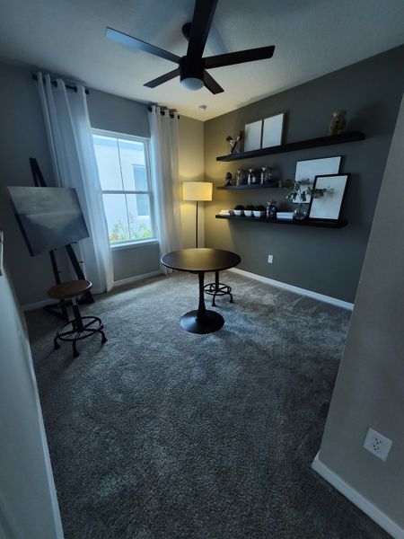 A cozy room with modern decor, featuring a sleek ceiling fan, artwork, shelves, and a round table for an inviting atmosphere. A cozy room with modern decor, featuring a sleek ceiling fan, artwork, shelves, and a round table for an inviting atmosphere.