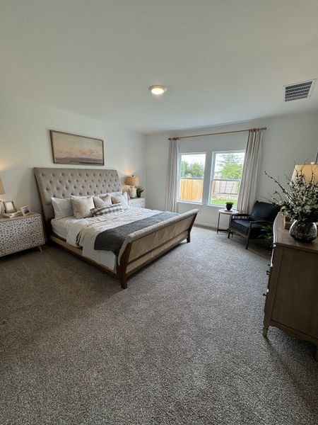 A spacious bedroom with plush carpeting, a tufted bed, and large windows letting in natural light. Cozy and inviting atmosphere.