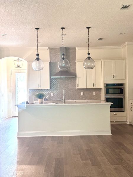A modern kitchen featuring white cabinetry, pendant lighting, and a chic tile backsplash with stainless steel appliances.