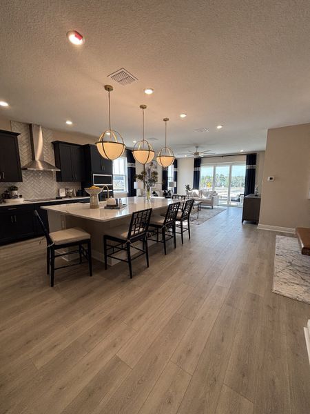 A cozy and stylish dining room featuring a sleek white table, upholstered chairs, and modern wall art, complemented by warm wood flooring in Crossroads at Kelly Park by Dream Finders Homes (Apopka, FL).