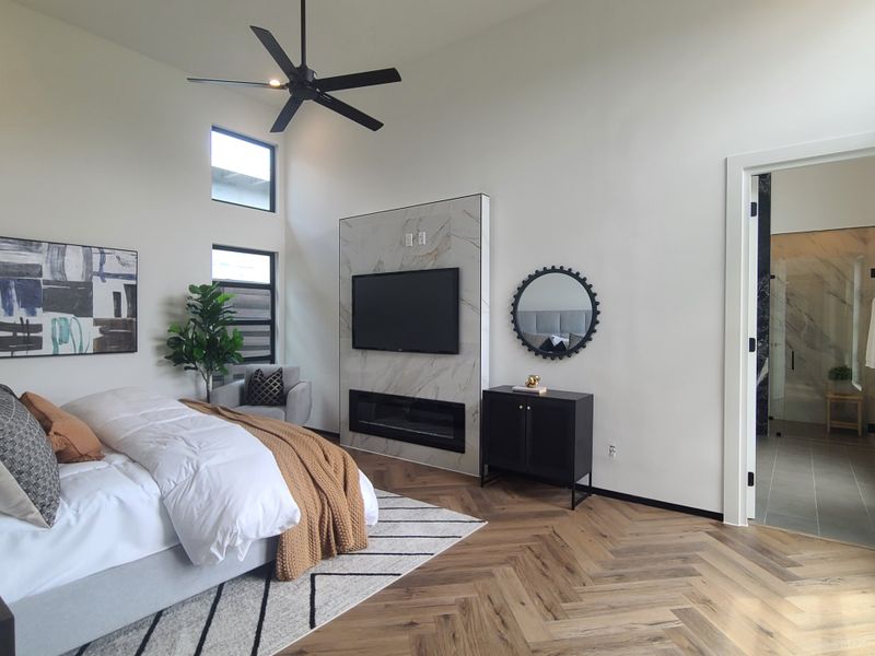 A chic bedroom with herringbone wood floors, modern art, and a cozy fireplace beside a stylish seating area.