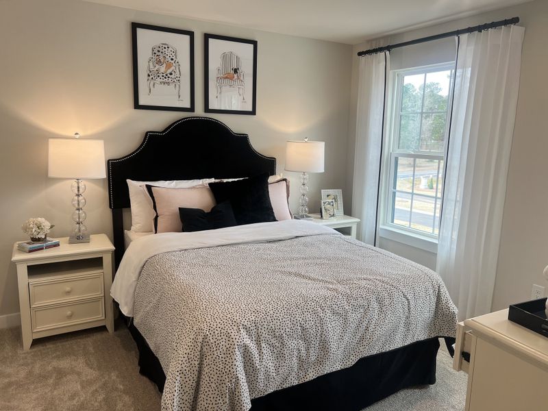 A cozy bedroom featuring a plush bed with patterned bedding, elegant lamps, and chic wall art, bathed in natural light.
