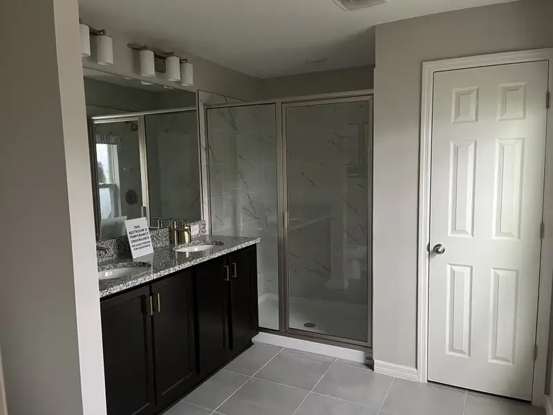 A modern bathroom featuring dual sinks, granite countertop, and a glass-enclosed shower.