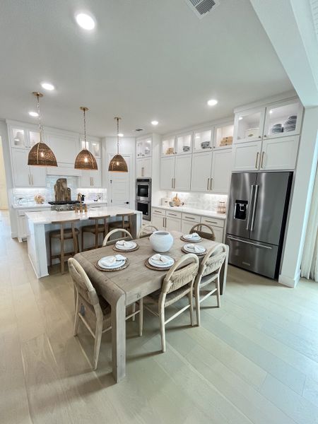 A bright kitchen with pendant lights, a rustic dining table, sleek cabinetry, and stainless steel appliances. A bright kitchen with pendant lights, a rustic dining table, sleek cabinetry, and stainless steel appliances.