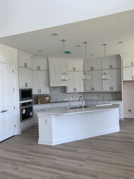 A spacious kitchen with sleek white cabinetry, a large island, and elegant pendant lighting, featuring light wood flooring.