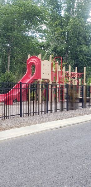 A vibrant playground with a red slide enclosed by a fence in Chestnut Grove by Starlight Homes (Douglasville, GA).