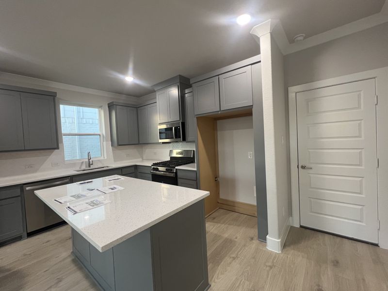 A modern kitchen featuring sleek gray cabinetry, a spacious island, and stainless steel appliances with elegant lighting.
