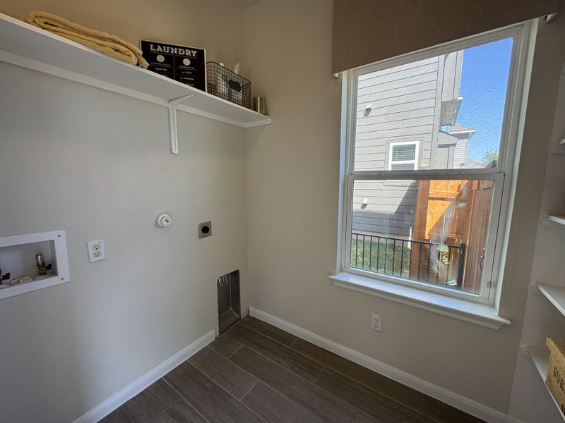A bright laundry room with a large window, wall shelves, and modern tile flooring. A bright laundry room with a large window, wall shelves, and modern tile flooring.