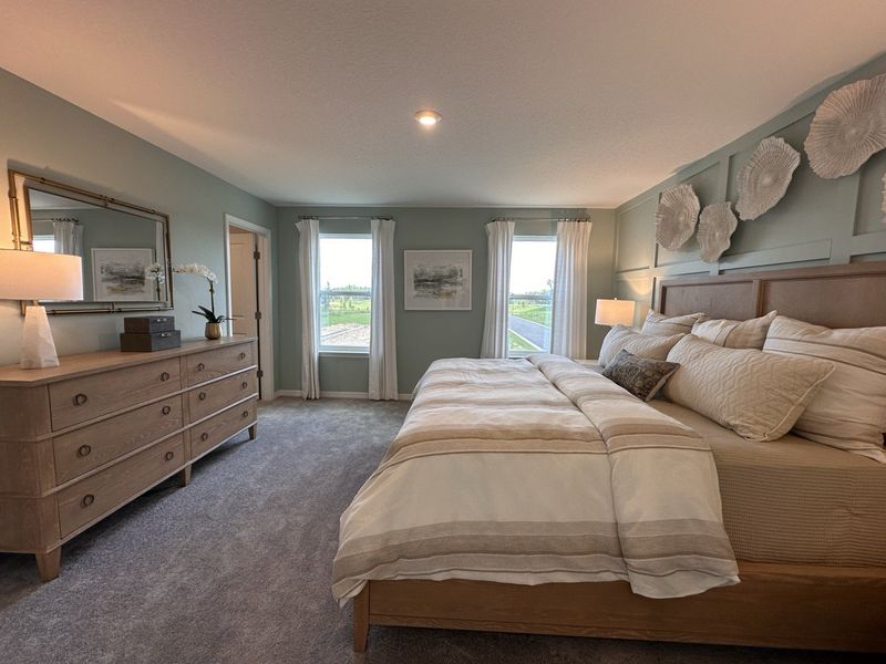 A serene bedroom with pastel walls, elegant decor, a cozy bed, and large windows offering ample natural light.