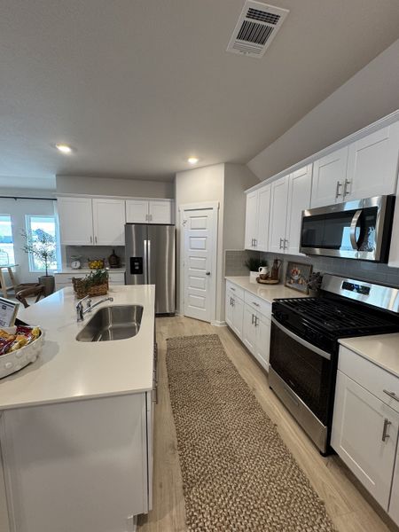 A modern kitchen with sleek white cabinets, stainless steel appliances, and a stylish, woven rug.