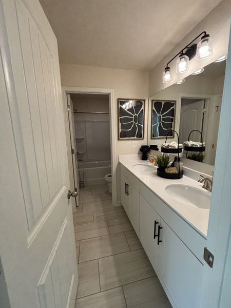 A modern bathroom featuring twin sinks, stylish artwork, and sleek light fixtures.