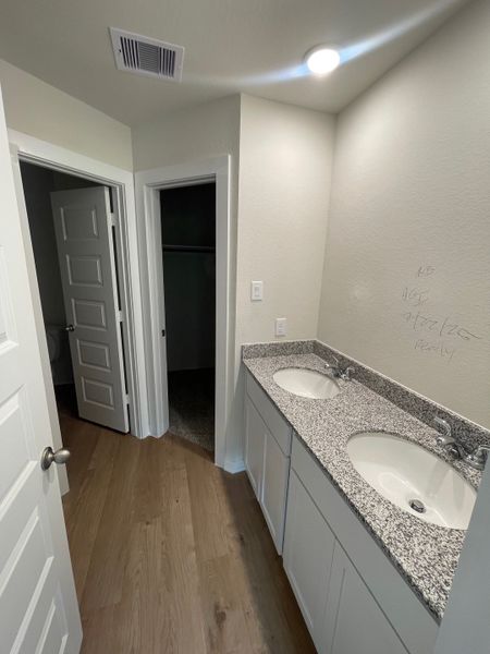 A modern bathroom featuring dual sinks, granite countertops, and sleek wood flooring.