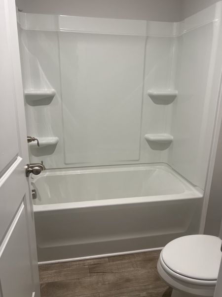 A sleek bathroom with a minimalist white tub, elegant shelving, and wood-look flooring. A sleek bathroom with a minimalist white tub, elegant shelving, and wood-look flooring.