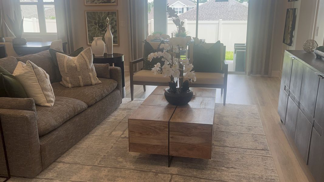 A cozy living area featuring a gray sofa, wooden coffee table, and elegant decor with natural light pouring through large windows.