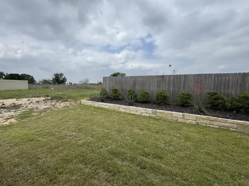 A serene backyard with lush greenery, bordered by a wooden fence and stone accent wall in Willowbrook by Scott Felder Homes (New Braunfels, TX). A serene backyard with lush greenery, bordered by a wooden fence and stone accent wall in Willowbrook by Scott Felder Homes (New Braunfels, TX).