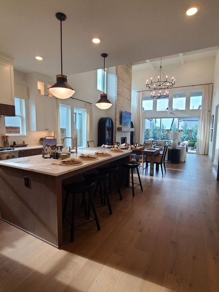 A modern open-concept living space with a stylish kitchen, island seating, high ceilings, and elegant lighting.