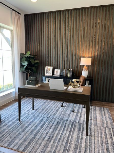 A modern home office featuring a wooden accent wall, sleek desk, and ample natural light from a large window.