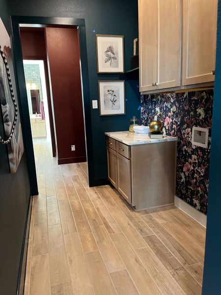 A chic hallway with wooden floors, floral wallpaper, and light cabinetry accentuated by framed botanical prints.