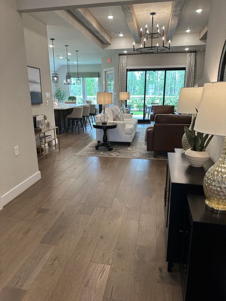 An elegant open-concept living area with hardwood floors, stylish lighting, and large windows overlooking a lush view.