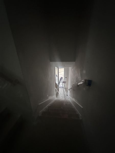A dimly lit stairway leading to a construction area with a ladder, framed by white walls.