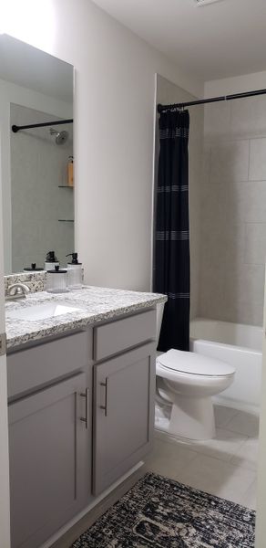 A modern bathroom featuring a granite-topped vanity, sleek cabinetry, and a classic shower curtain.