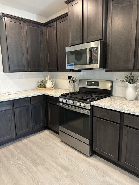 A modern kitchen with dark wood cabinets, granite countertops, stainless steel appliances, and light wood flooring.