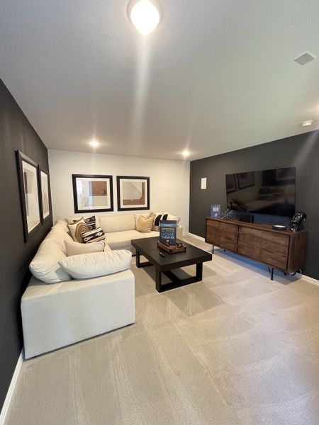 A cozy media room with a plush white sectional, dark accent wall, and sleek entertainment center. Perfect for relaxing.