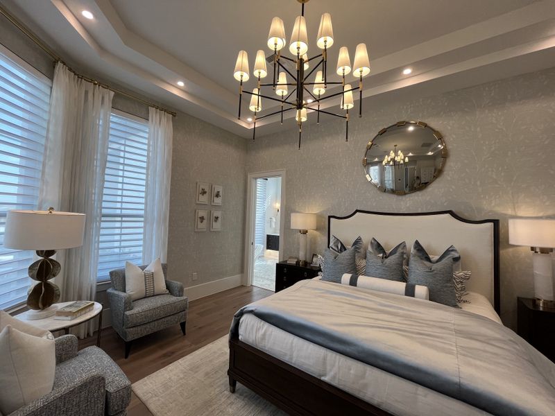 A luxurious bedroom featuring elegant lighting, plush bedding, and cozy seating in a serene, softly-lit ambiance.
