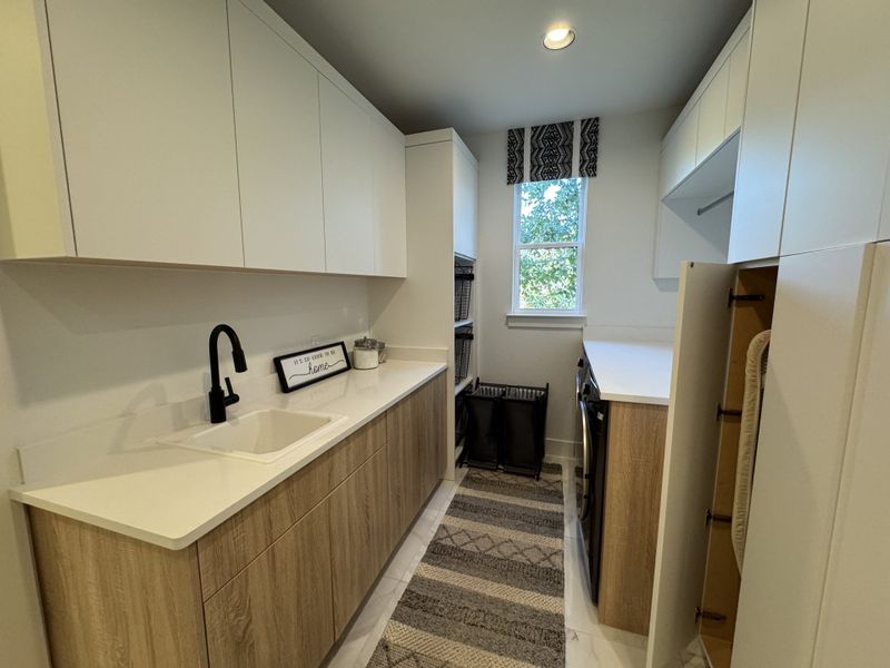 A sleek laundry room with wood accents, ample storage, and natural light filtering through a window.