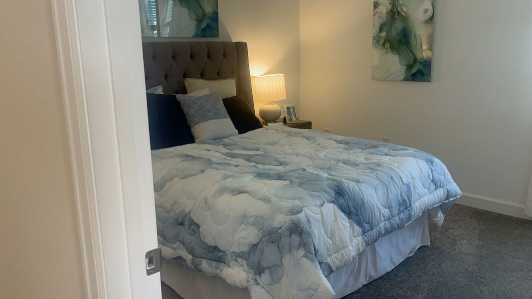 A cozy bedroom with a tufted headboard, blue-toned bedding, abstract artwork, and soft lighting.