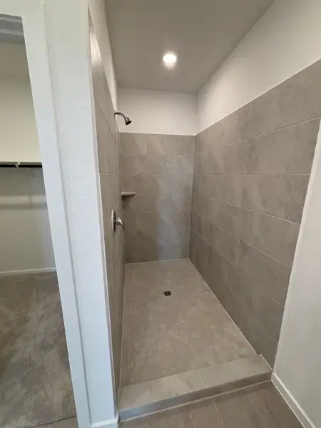 A modern shower with gray tiling and sleek fixtures opening into a carpeted closet area.