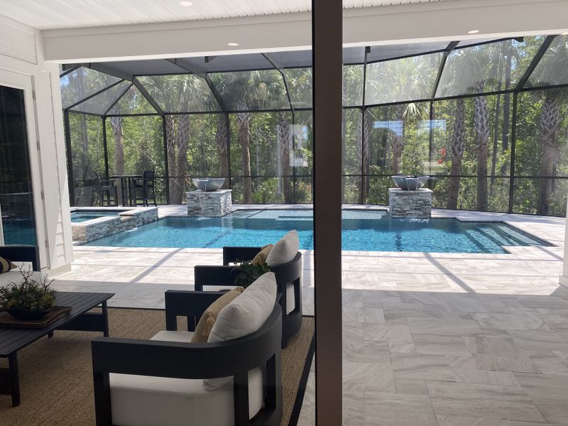 Luxurious screened-in pool area with modern seating, elegant tiles, and serene views of lush surroundings.