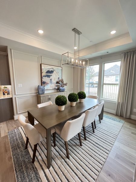 A modern dining room with a sleek table, stylish chairs, and elegant lighting on a striped rug. A modern dining room with a sleek table, stylish chairs, and elegant lighting on a striped rug.