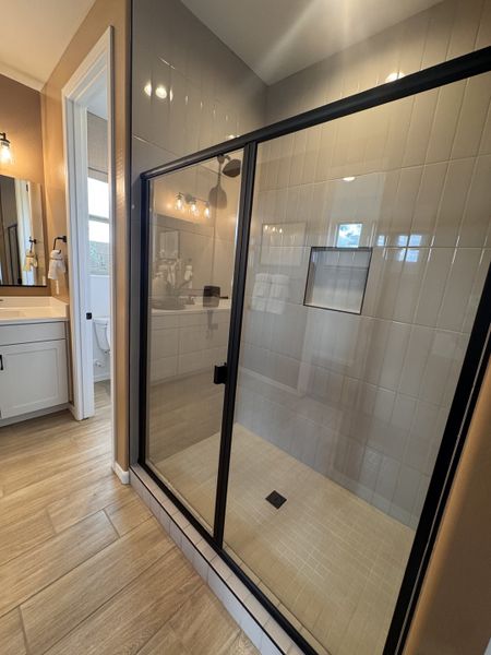 A modern bathroom with a glass-enclosed shower, wood-look tile floors, and a sleek vanity with stylish lighting.