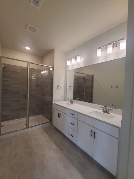 A sleek bathroom featuring a spacious glass shower, dual sinks, and modern lighting with elegant finishes throughout.