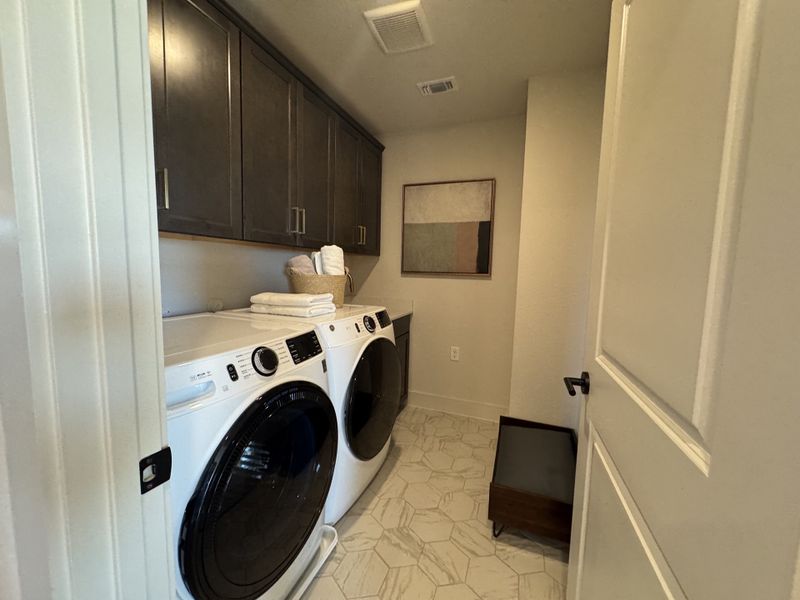 A functional laundry room with modern appliances, sleek cabinetry, and stylish tile flooring.