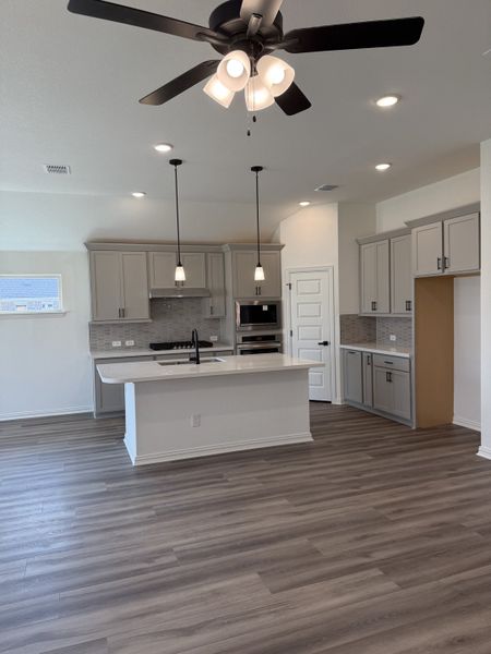 A modern kitchen with sleek cabinetry, an island, pendant lighting, and wood-look flooring. A modern kitchen with sleek cabinetry, an island, pendant lighting, and wood-look flooring.