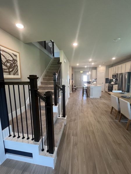 A modern interior featuring a spacious hallway with wooden flooring, elegant staircase, and chic kitchen-dining area. A modern interior featuring a spacious hallway with wooden flooring, elegant staircase, and chic kitchen-dining area.