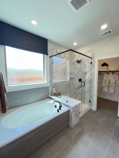 A modern bathroom featuring a spacious bathtub, glass shower with marble accents, and elegant tile flooring.