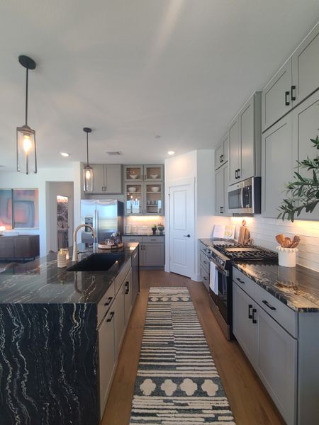Modern kitchen with sleek black countertops, gray cabinets, warm wood flooring, and pendant lighting. Modern kitchen with sleek black countertops, gray cabinets, warm wood flooring, and pendant lighting.