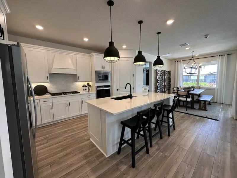 A modern kitchen with white cabinetry, a large island, and pendant lighting, opening to a cozy dining area with natural light.