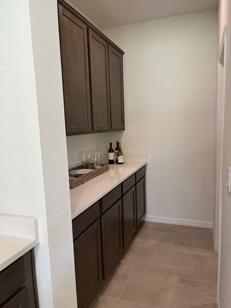 A sleek butler’s pantry with dark wood cabinetry, white countertops, and elegant tile flooring.