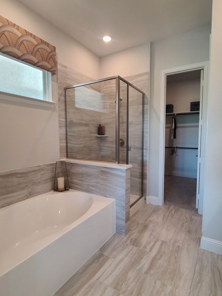 A modern bathroom with a sleek glass shower, white bathtub, elegant tiling, and contemporary window treatment.